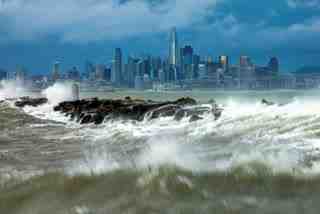 Waves crash over a breakwater in Alameda, Calif., with the San Francisco skyline in the background on Sunday, Feb. 4, 2024. High winds and heavy rainfall are impacting the region.